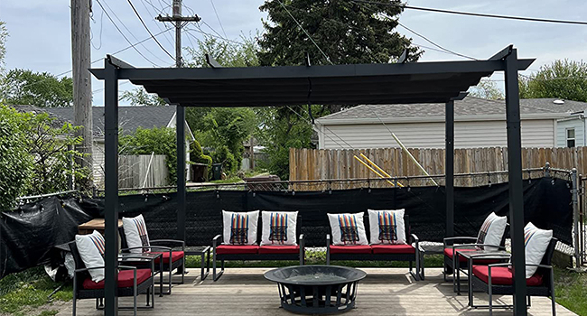 Terrasse extérieure avec pergola noire, terrasse en bois et ensemble de sièges comprenant des chaises rembourrées rouges et des canapés disposés autour d'une table noire basse