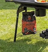Sac à charbon suspendu à une remorque de camping en métal noir, support de rangement monté sur attelage avec contenant pour aliments sur le dessus, exposé dans un cadre extérieur gazonné.